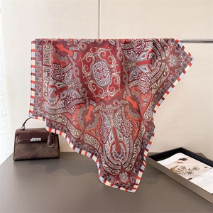Classic red paisley silk square scarf with striped border hanging on display