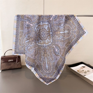 Detail of paisley pattern silk scarf with blue and lilac tones draped on a leather bag
