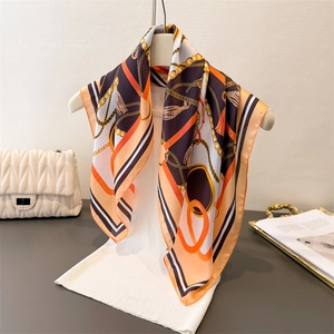 Elegant silk scarf with orange and black chain print draped on a white display stand