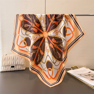 Close-up of silk scarf with orange chain print draped over a luxury bag background
