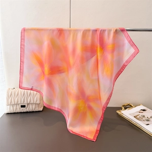 Close-up of floral print silk scarf with delicate pink edges hanging on silver rack