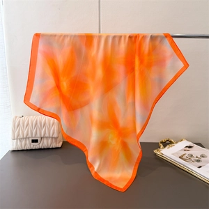 Detail of silk-like floral square scarf with bright orange border and draped texture
