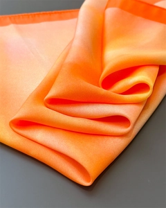 Detailed view of luxury silk scarf showing orange gradient texture and soft satin folds