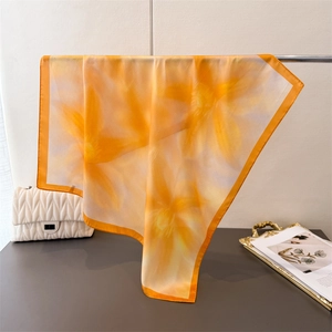 Floral print silk scarf in yellow and orange hanging on a silver metal display stand