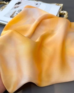 Detail of silk-like scarf with orange gradient and glossy texture on gold tray
