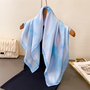 Elegant square silk scarf with blue and white cloud print pattern displayed on a bag