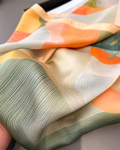 Detailed view of silk-like scarf with abstract geometric print in orange and olive green