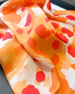 Détail d'un foulard en soie à imprimé léopard avec texture lisse et tons rouge-orange