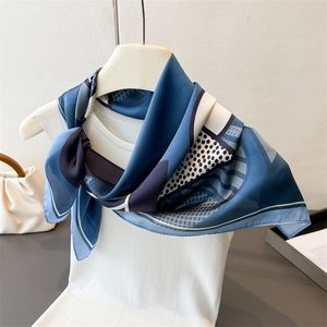 Close-up of a blue geometric silk scarf styled on a white vest with elegant patterns