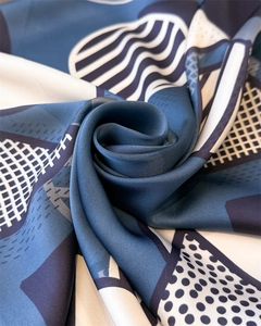 Close-up of geometric silk scarf with navy dots and stripes showing smooth satin texture