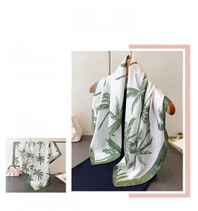 Detailed close-up of a white silk scarf with green palm leaf print and fine green edges
