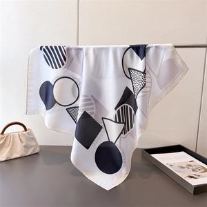 Detail of geometric silk scarf hanging elegantly with a beige pleated handbag
