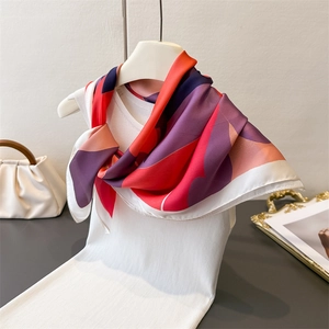 Detail of silk-like square scarf with geometric print draped over a white knit top