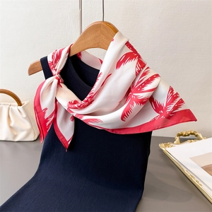 Close-up of a white silk scarf with red palm tree prints tied on a black knitted top