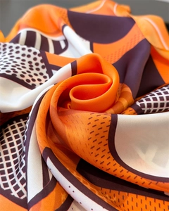 Close-up of bright orange geometric silk-like scarf showing texture and glossy finish