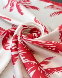 Detailed close-up of premium satin silk scarf with elegant red palm leaf tropical print