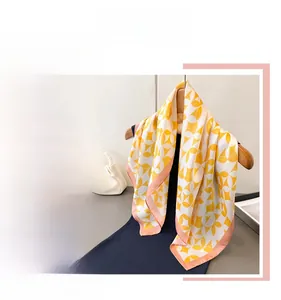 Detail view of yellow floral pattern faux silk scarf with elegant orange border