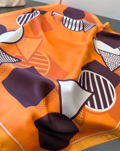 Macro detail of geometric silk scarf fabric with orange and purple patterns and soft drapes