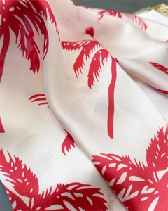 Detailed macro view of silky cream scarf featuring vibrant red tropical palm tree prints