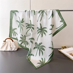 Detail of silk-like white scarf with green palm tree print draped on metal rack