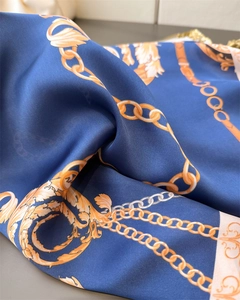 Macro detail of silk-like blue scarf with luxury golden chain and scroll patterns