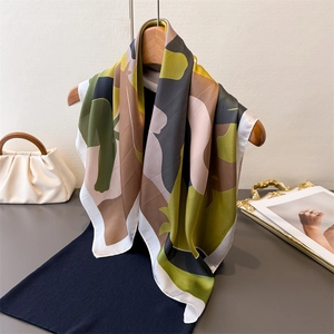 Elegant geometric olive green satin silk scarf draped on a hanger with a dark blue outfit