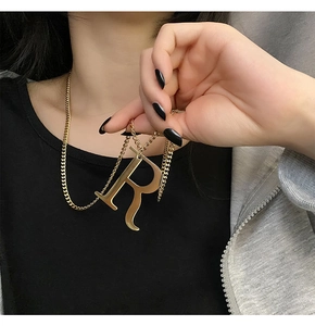 Detailed close-up of a large gold letter R pendant necklace on a chain worn by a model