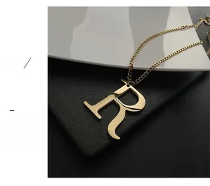 Macro shot of polished gold letter R pendant with elegant thin chain on a textured background