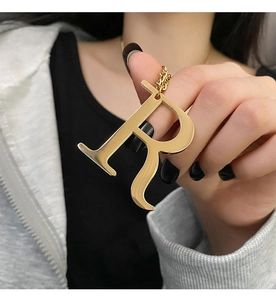 Close-up of a large polished gold R-letter pendant necklace held by a hand