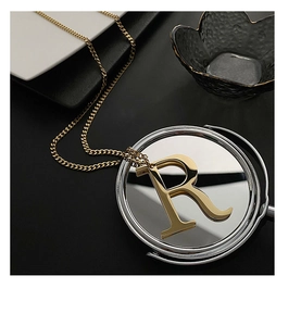 Close-up of golden R letter pendant on curb chain reflected in a round mirror surface