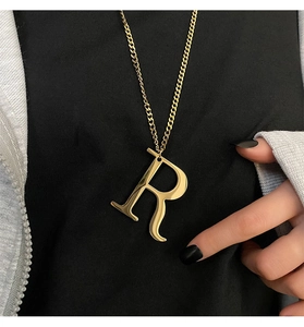 Close-up of golden letter R pendant necklace on person wearing casual clothing