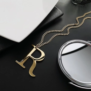 Modern gold-plated letter R pendant necklace displayed on a textured black surface