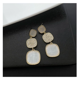 Close-up of geometric tiered earrings with sparkling rhinestones and white pearl finish