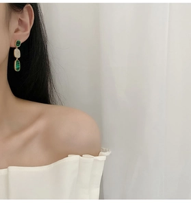 Close-up of elegant gold tiered drop earrings with green stones on a female model