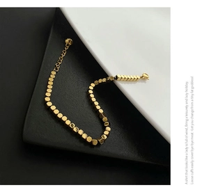 Detail of a minimalist gold cube beaded bracelet featuring a lobster clasp and extension chain