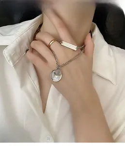 Detail of silver chain necklace with rectangle plate and coin pendant on a white shirt