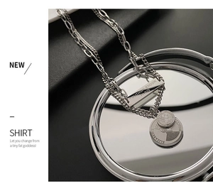 Detail of layered titanium steel necklace with engraved bar and vintage coin pendants