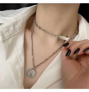 Close-up of silver double-layered necklace with Queen Elizabeth coin pendant and logo tag