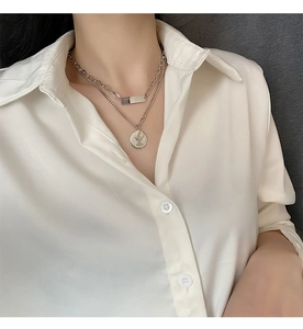 Detail of layered silver coin pendant necklace worn on a white silk shirt