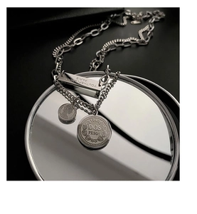 Silver double-layer titanium necklace with vintage coin pendants on a mirror surface