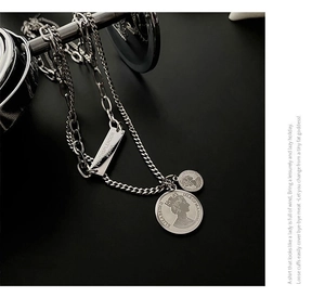 Detail of layered silver chain necklace with vintage coin pendants and engraved plate