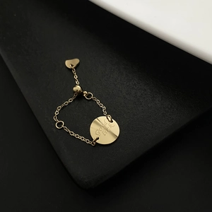 Détail de la bague chaîne dorée avec pendentif Good Luck et petit charm en cœur