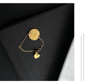 Détail d'une bague chaîne dorée avec pendentif pièce de monnaie et breloque cœur