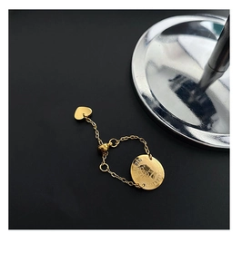 Détail d'une bague chaîne dorée ajustable avec pendentif pièce et petit charme cœur