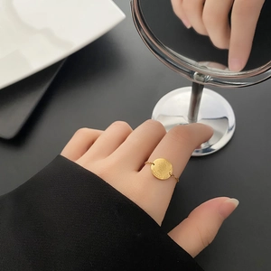Bague chaîne dorée avec pendentif pièce Elizabeth II portée sur fond noir minimaliste