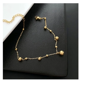 Detailed view of a gold beaded anklet with lobster clasp and adjustable metal chain