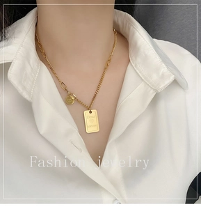 Detail of gold titanium necklace with engraved square pendant and circular luck charm