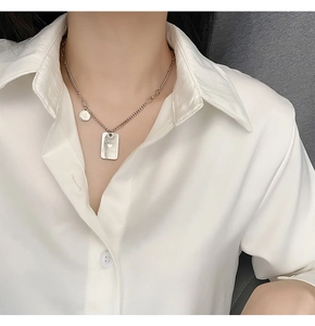 Detail of silver square and round pendants necklace worn on a white silk shirt