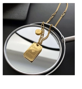 Macro detail of gold titanium steel necklace with engraved square pendant on a mirror