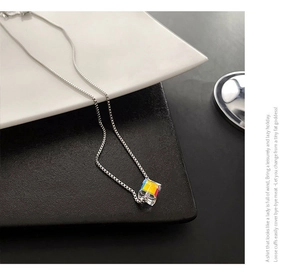 Dettaglio macro della catena in titanio argento con pendente a cubo geometrico colorato su piatto